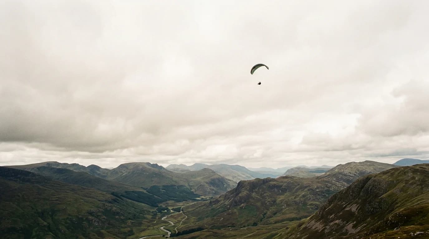 A paraglider crossing a heavy overcast above a long range of mountains.