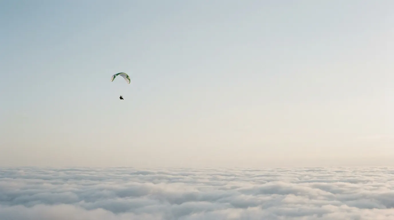 A paraglider drifting above an unbroken deck of cloud.